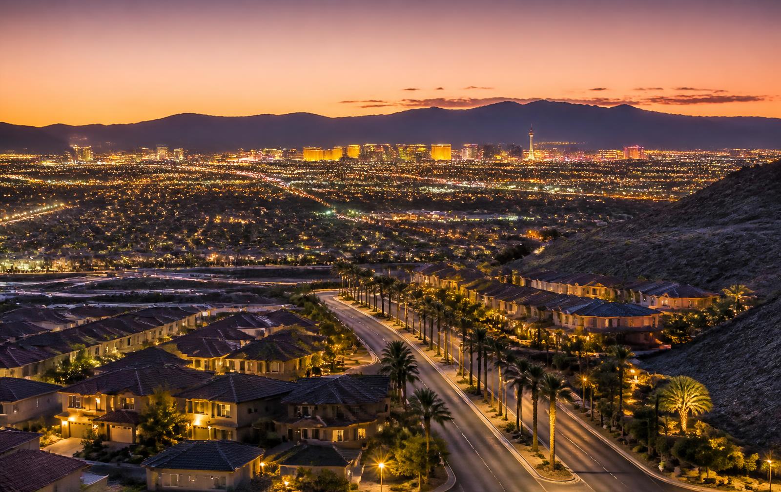 Evening view across a Las Vegas and Henderson valley neighborhood with city lights glowing toward the distant skyline.