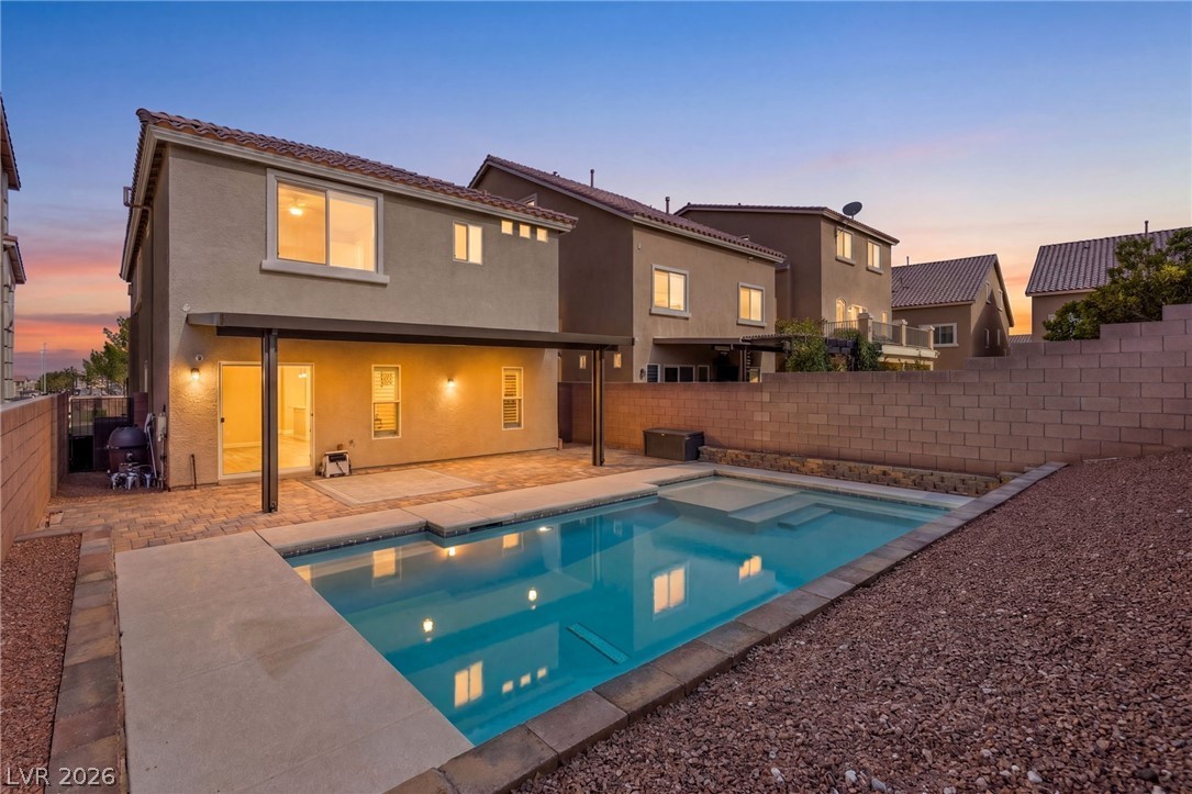 Backyard of 7187 Mann St, Las Vegas at dusk — two-story home with covered patio, pool and spa, and paver decking.