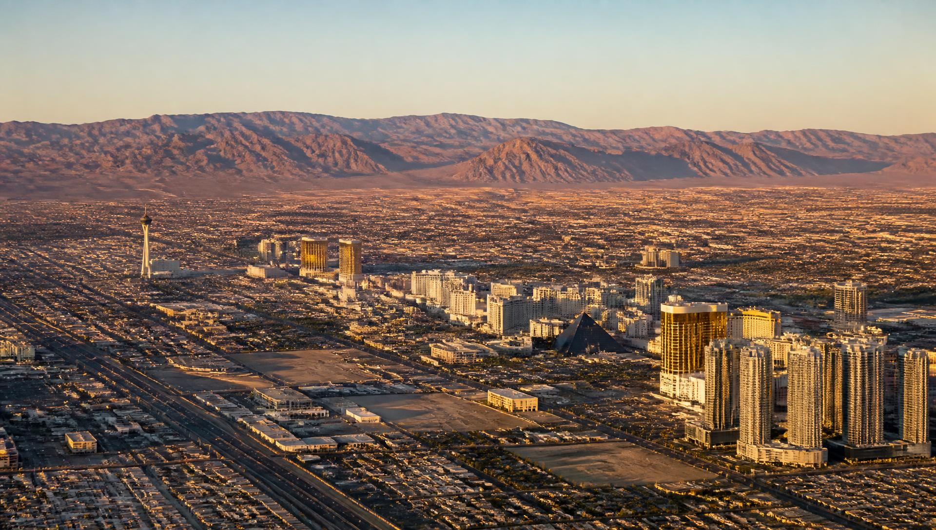 Wide aerial view of the Las Vegas valley at golden hour, the city grid spreading across the basin toward the surrounding mountain ranges.