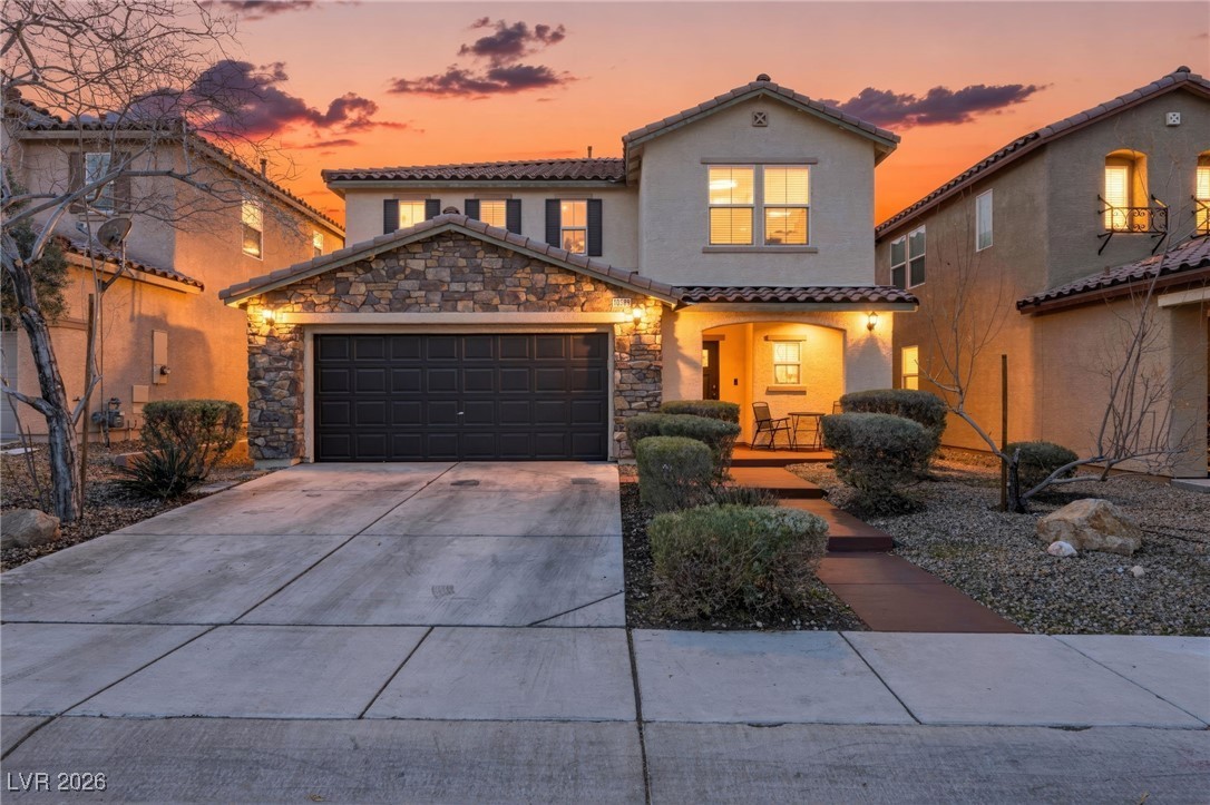 Front exterior of 10589 Natural Bridge St, Las Vegas at sunset — two-story home with stone-faced garage, tile roof, and desert landscaping.