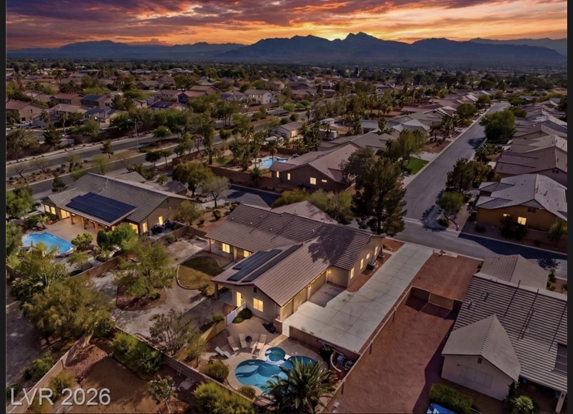 Aerial twilight photograph of 8088 Winchester Bluff St in Las Vegas and the surrounding single-story homes, with backyard pools and mountains on the horizon.