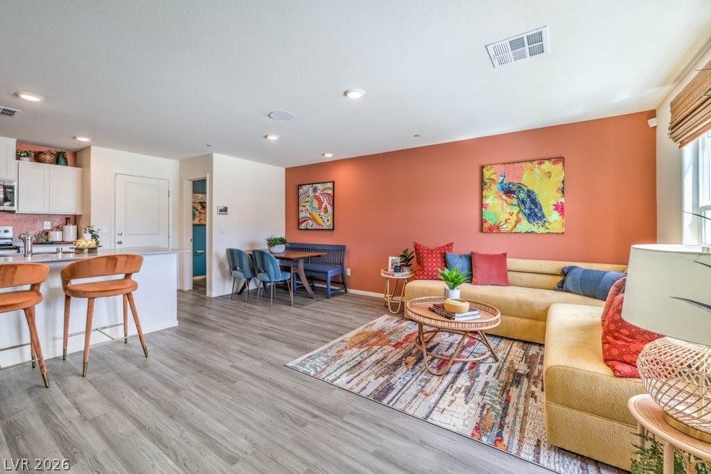 Interior of 1449 Pamela Springs Ln, North Las Vegas — open living and dining area with a terracotta accent wall, light wood-look flooring, and a kitchen breakfast bar.
